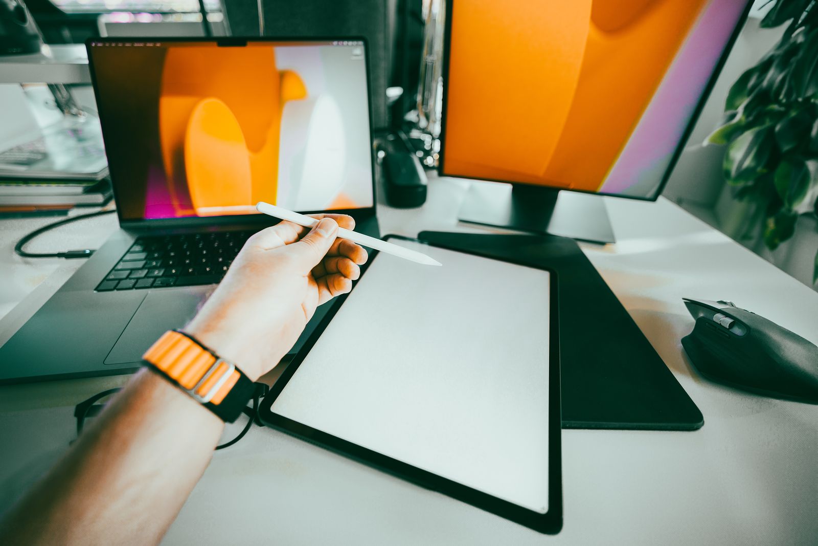 Hand using a stylus on a graphics tablet beside a laptop and monitor