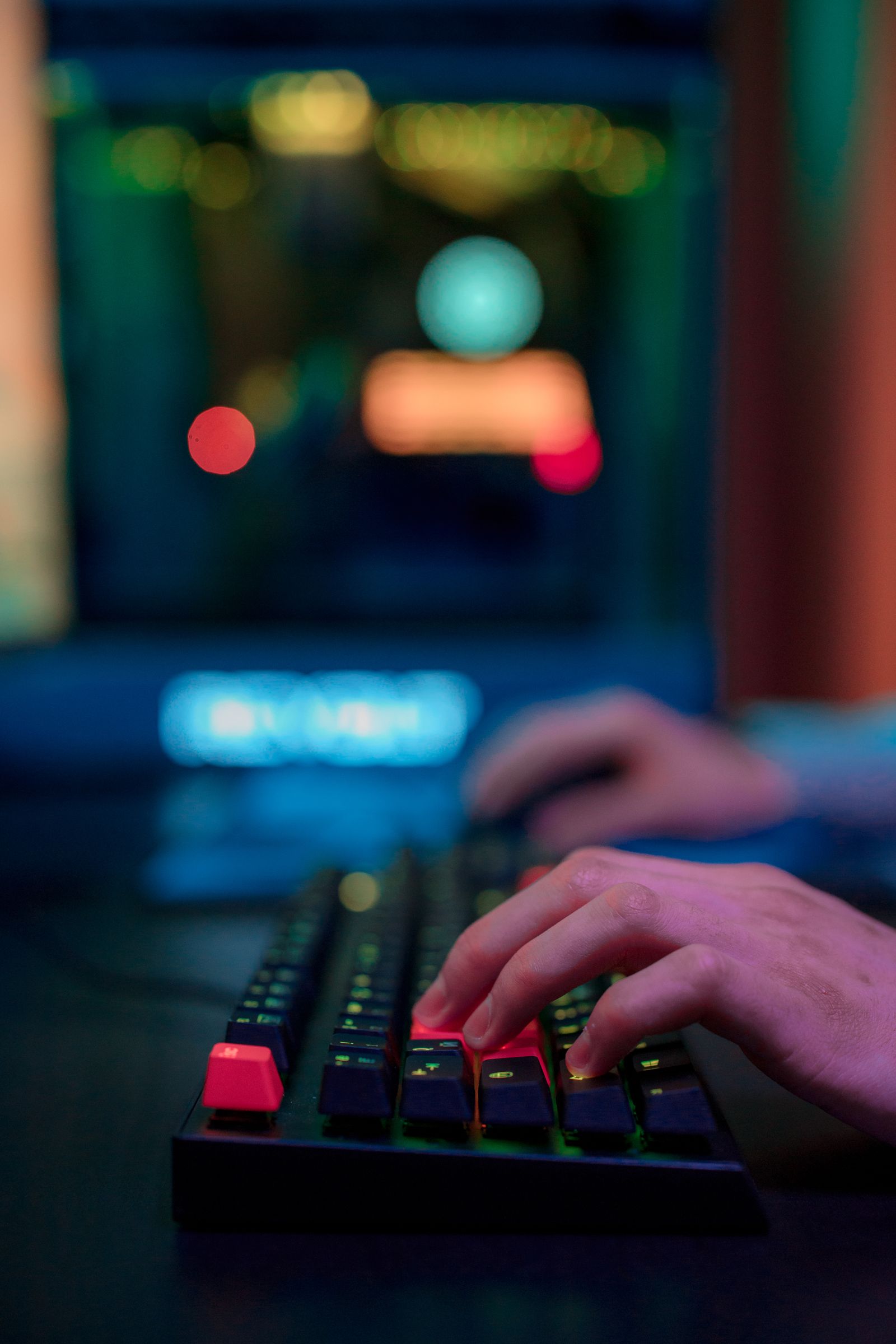 Hands on an RGB-lit keyboard with blurred screens behind