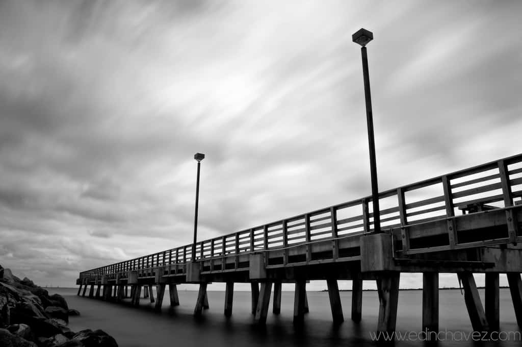 Black and white pier extending over water beneath a clouded sky
