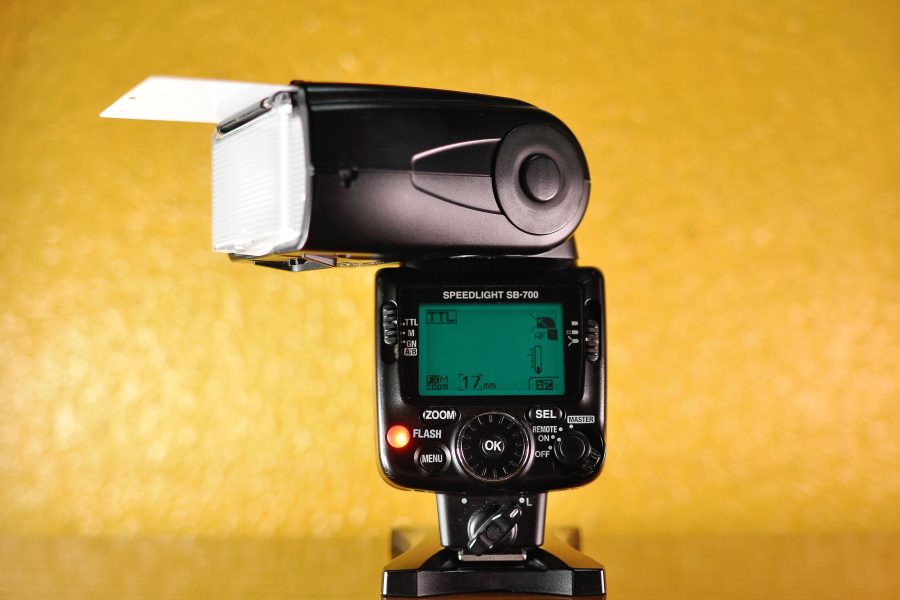 Nikon SB-700 speedlight on a stand against a yellow background (stock photo, illustrative)