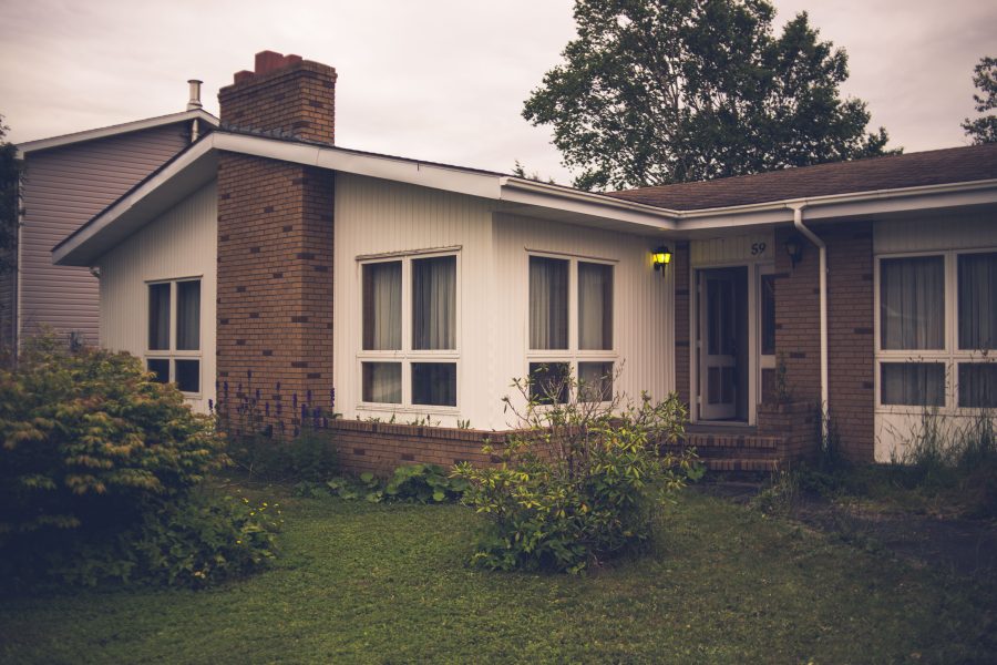 A suburban house with a brick chimney, white siding, and a front lawn under an overcast sky