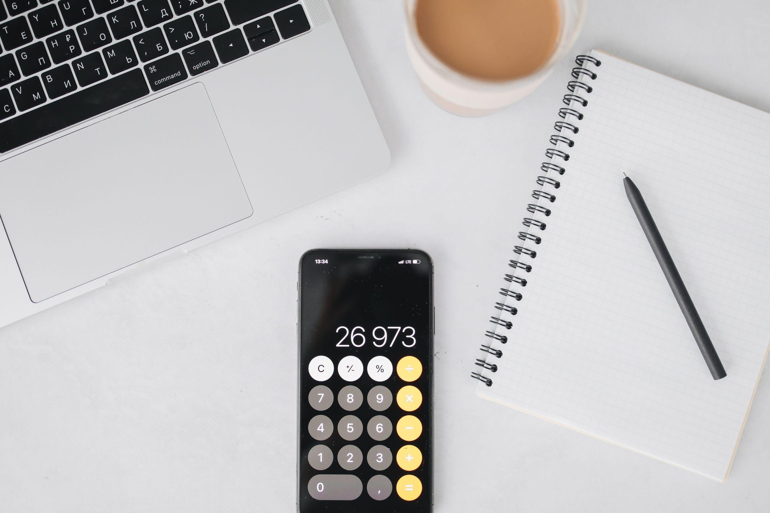 Phone calculator and notebook beside a laptop and coffee. (Stock photo, illustrative.)