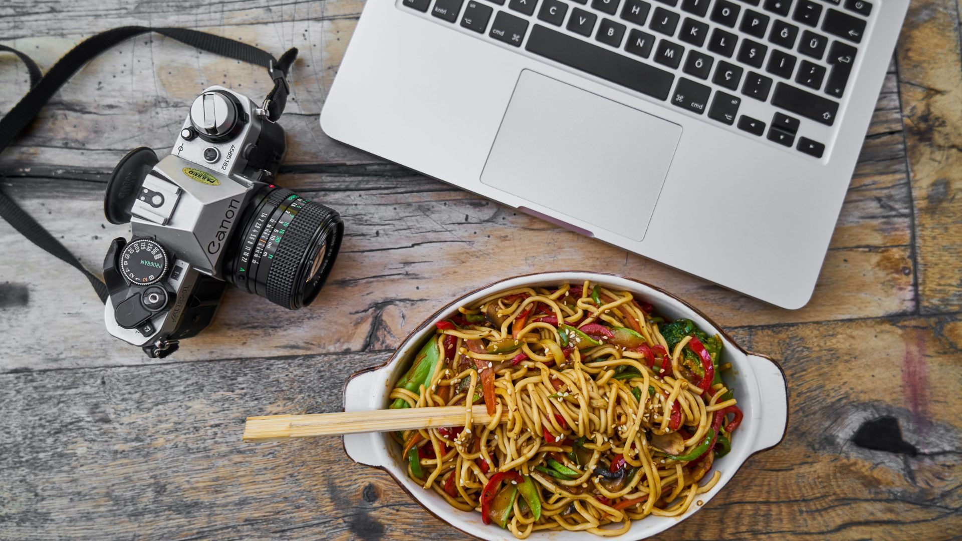 Film camera laptop and bowl of noodles on a wooden table. (Stock photo, illustrative.)