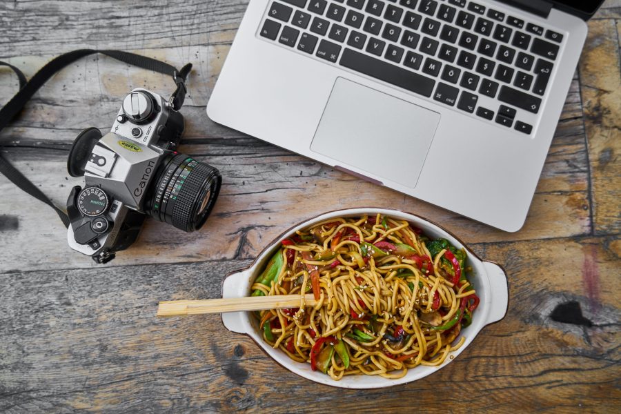 Film camera laptop and bowl of noodles on a wooden table. (Stock photo, illustrative.)