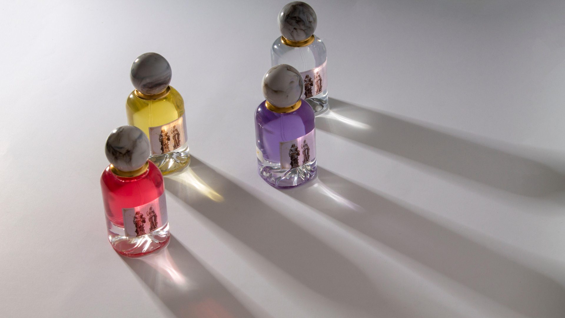 Colorful perfume bottles casting long shadows on a white surface. (Stock photo, illustrative.)