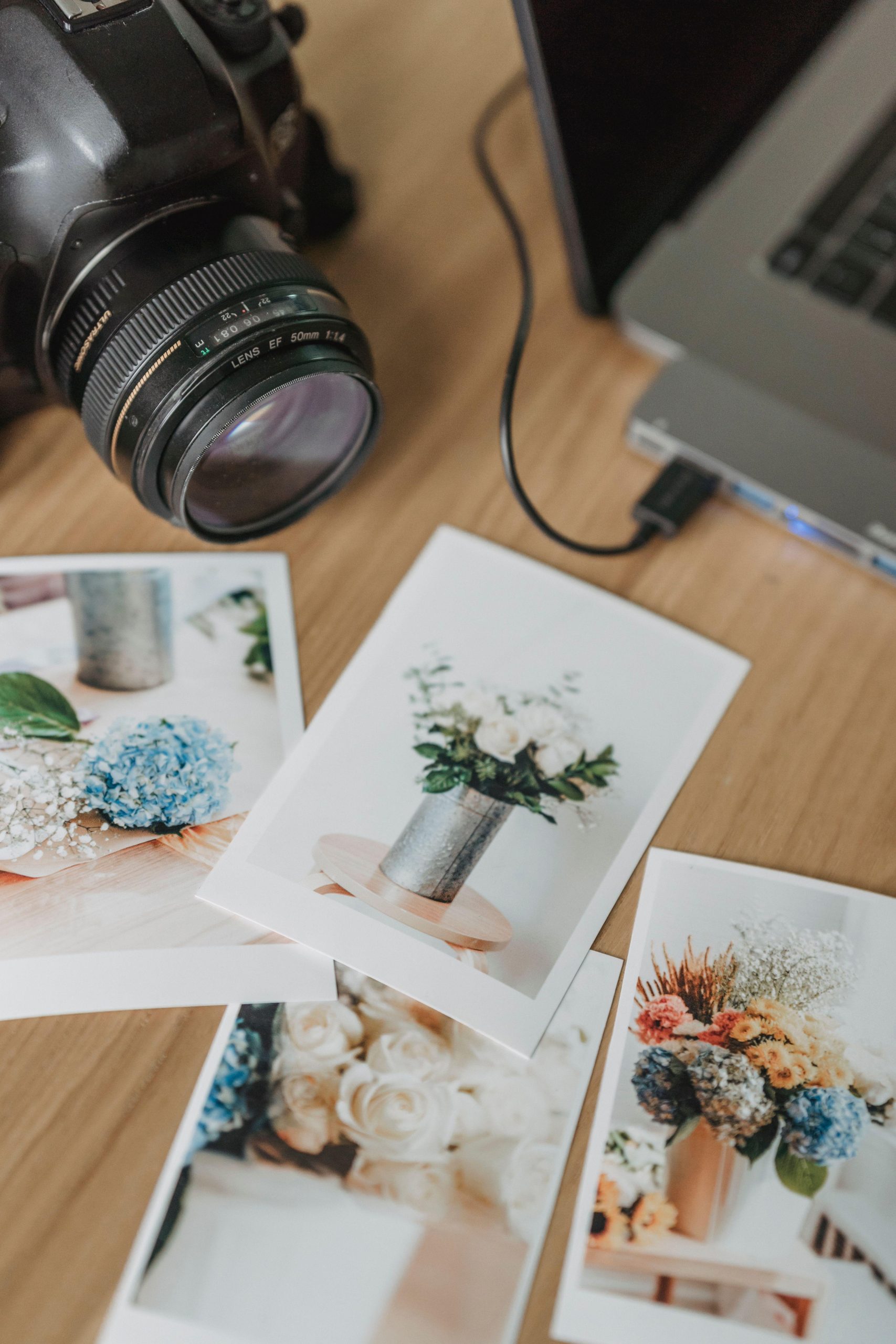 Camera beside printed flower photographs on a wooden table. (Stock photo, illustrative.)