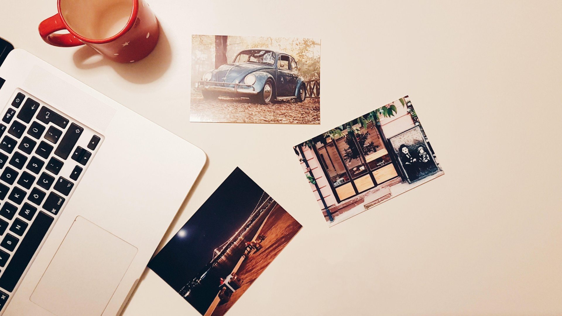 Printed photographs beside a laptop and red mug on a light desk. (Stock photo, illustrative.)