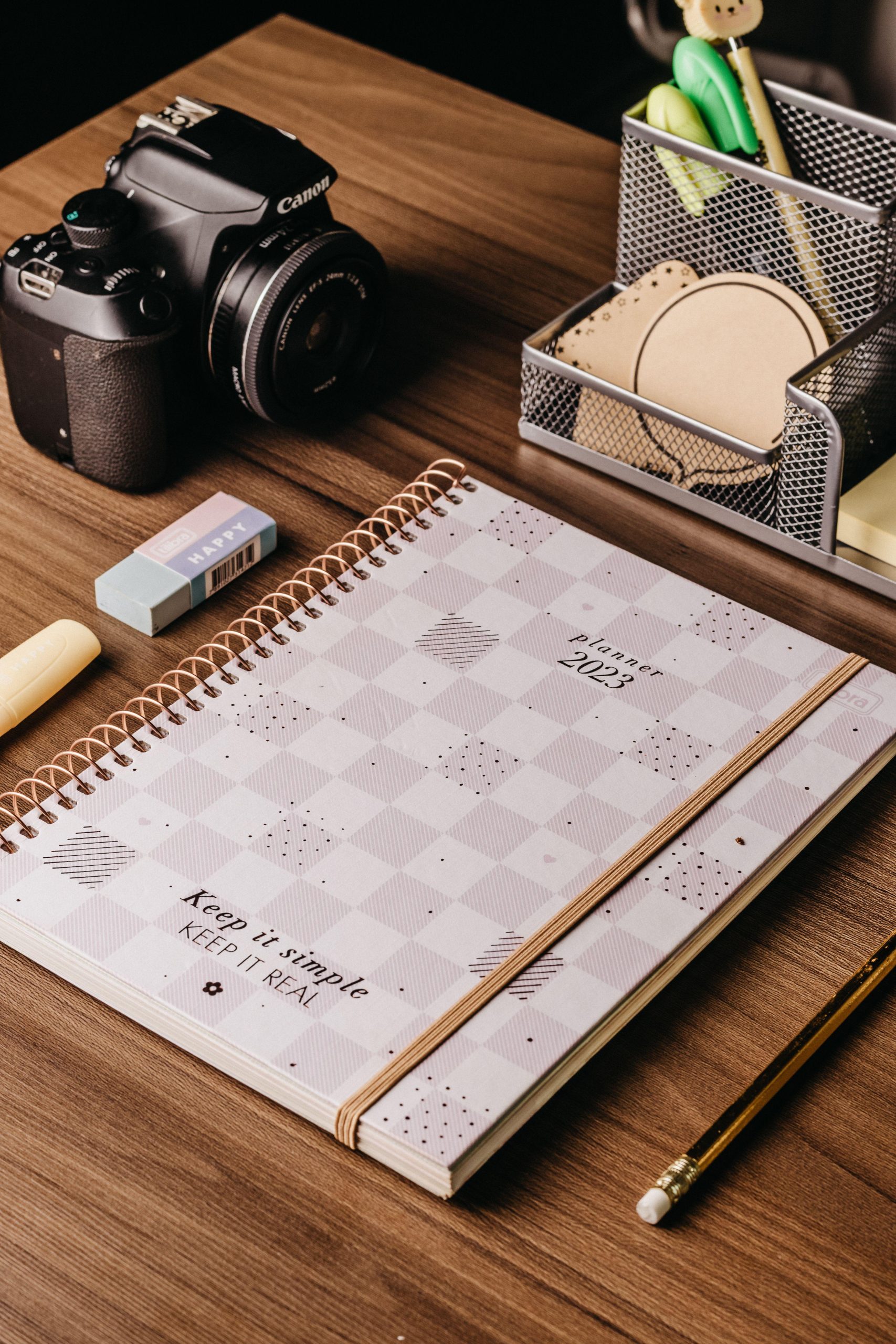 Planner and camera beside stationery on a wooden desk. (Stock photo, illustrative.)