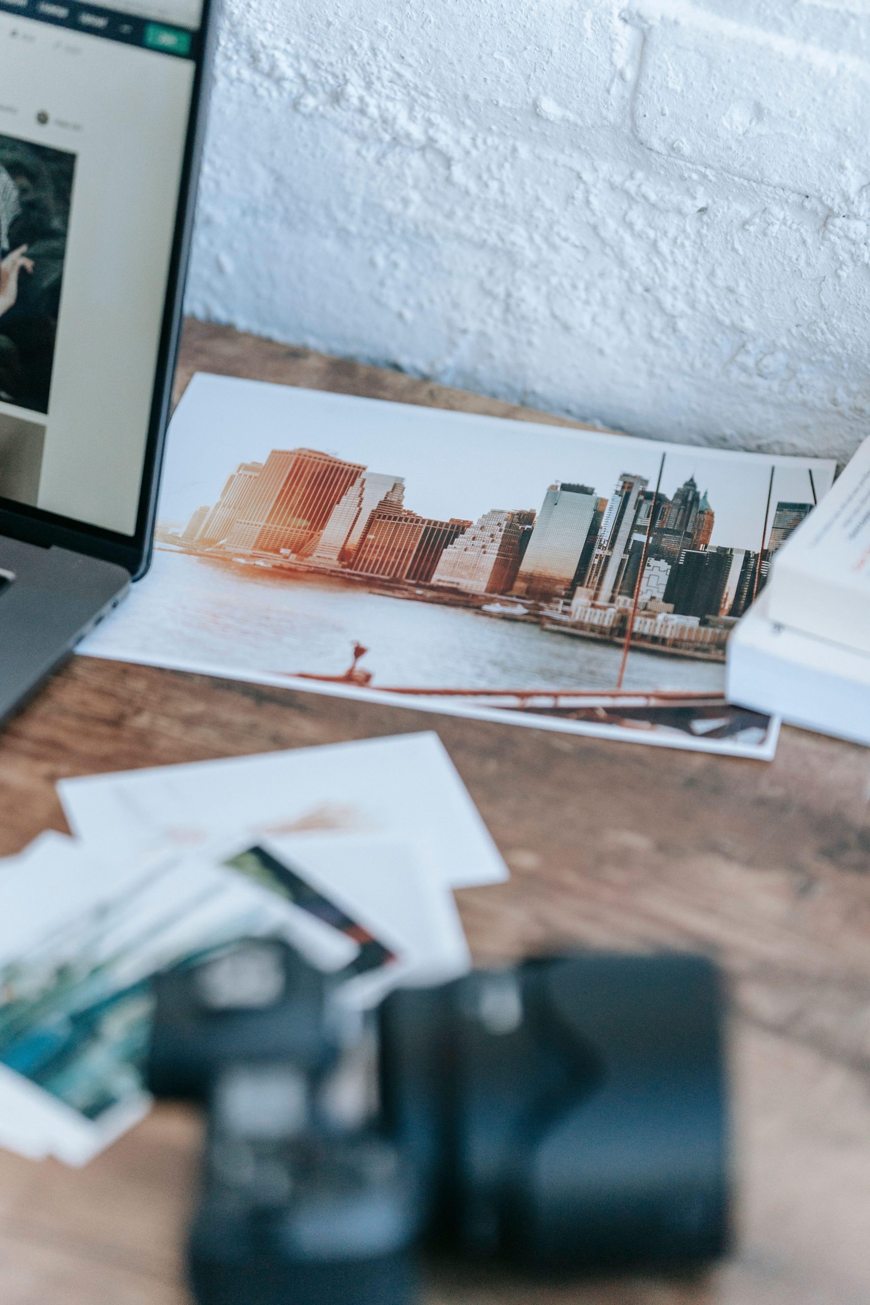 Printed waterfront cityscape photographs beside a laptop and camera. (Stock photo, illustrative.)