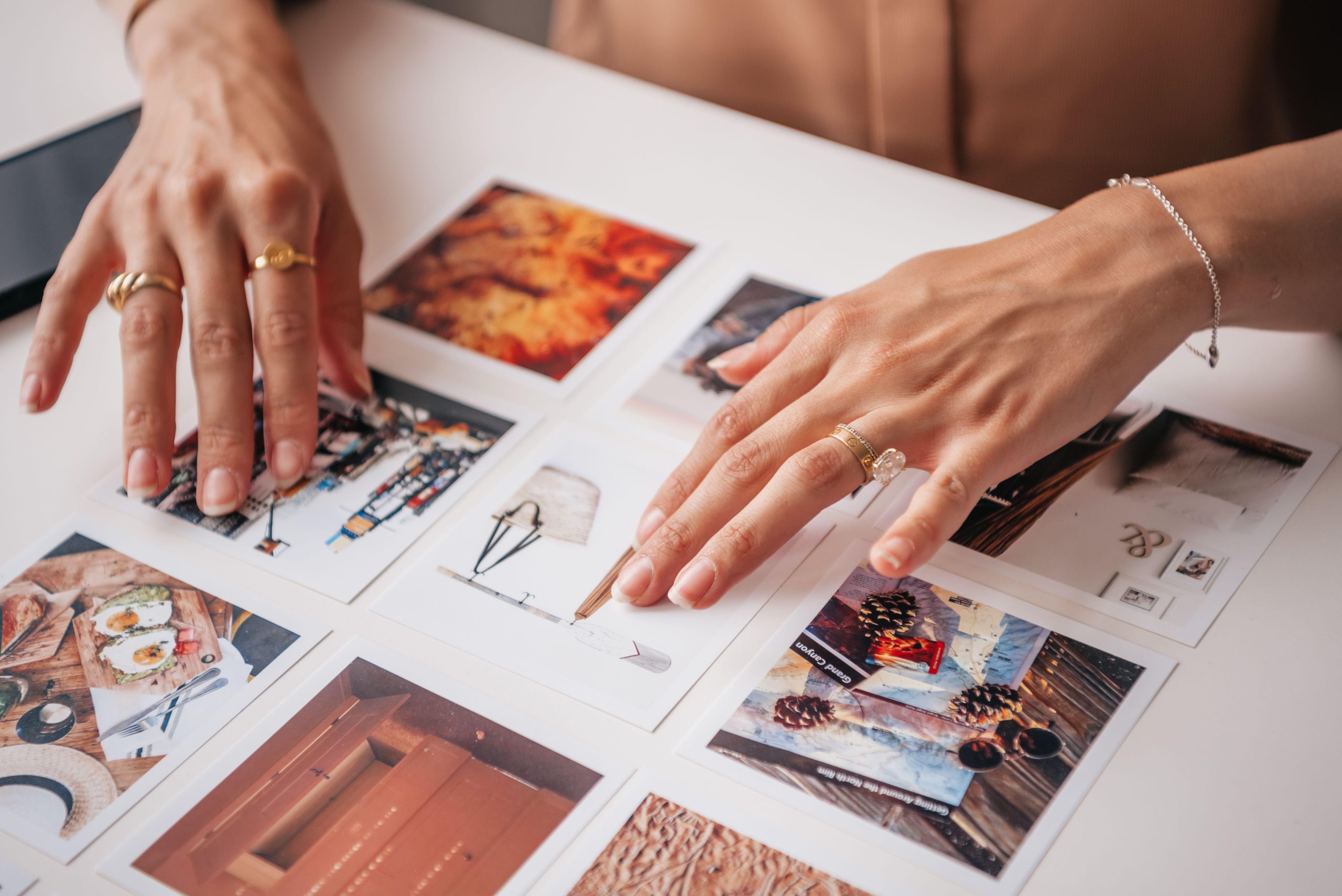Anonymous hands arranging printed photographs on a white table. (Stock photo, illustrative.)