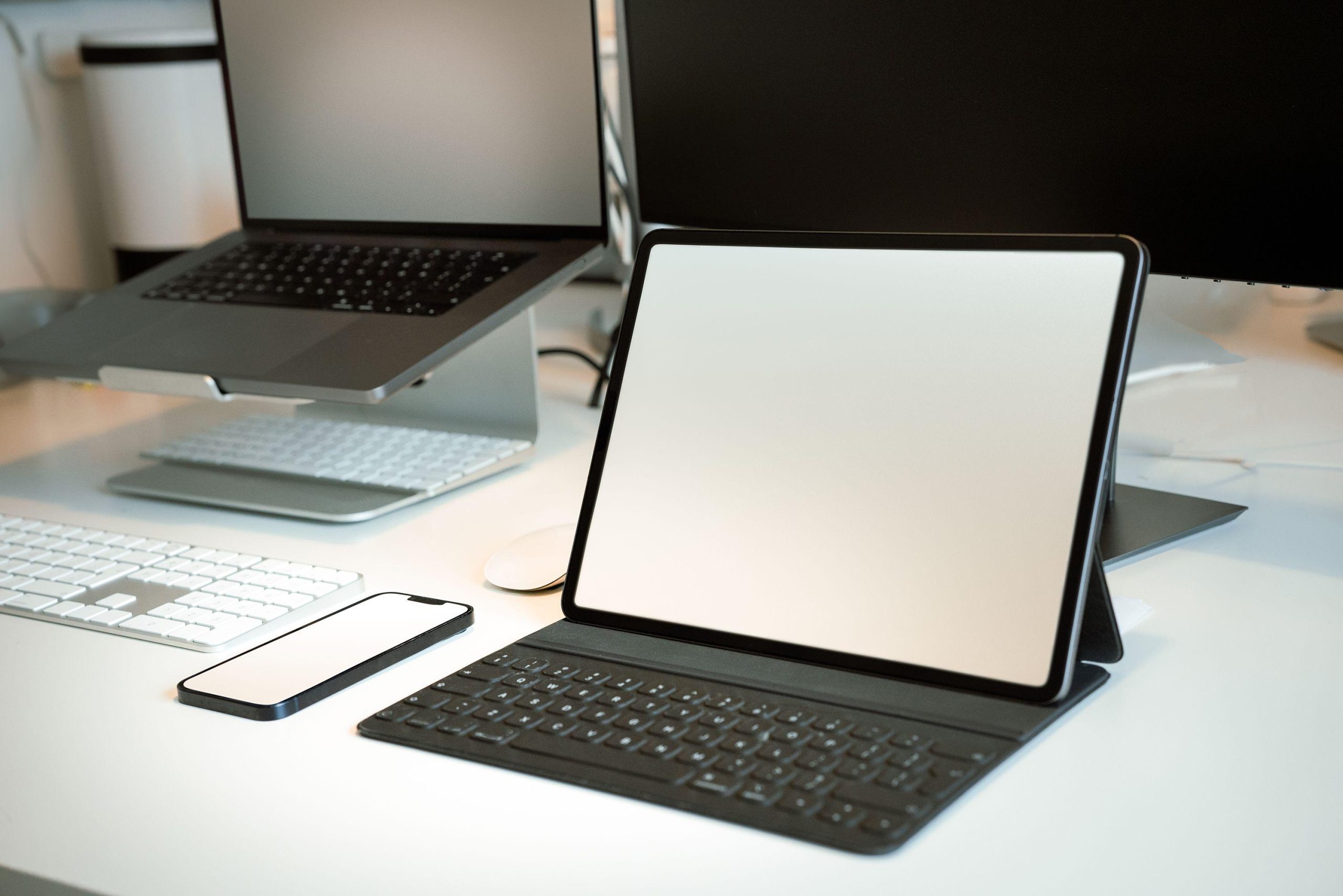 Tablet with keyboard and laptops on a bright desk. (Stock photo, illustrative.)