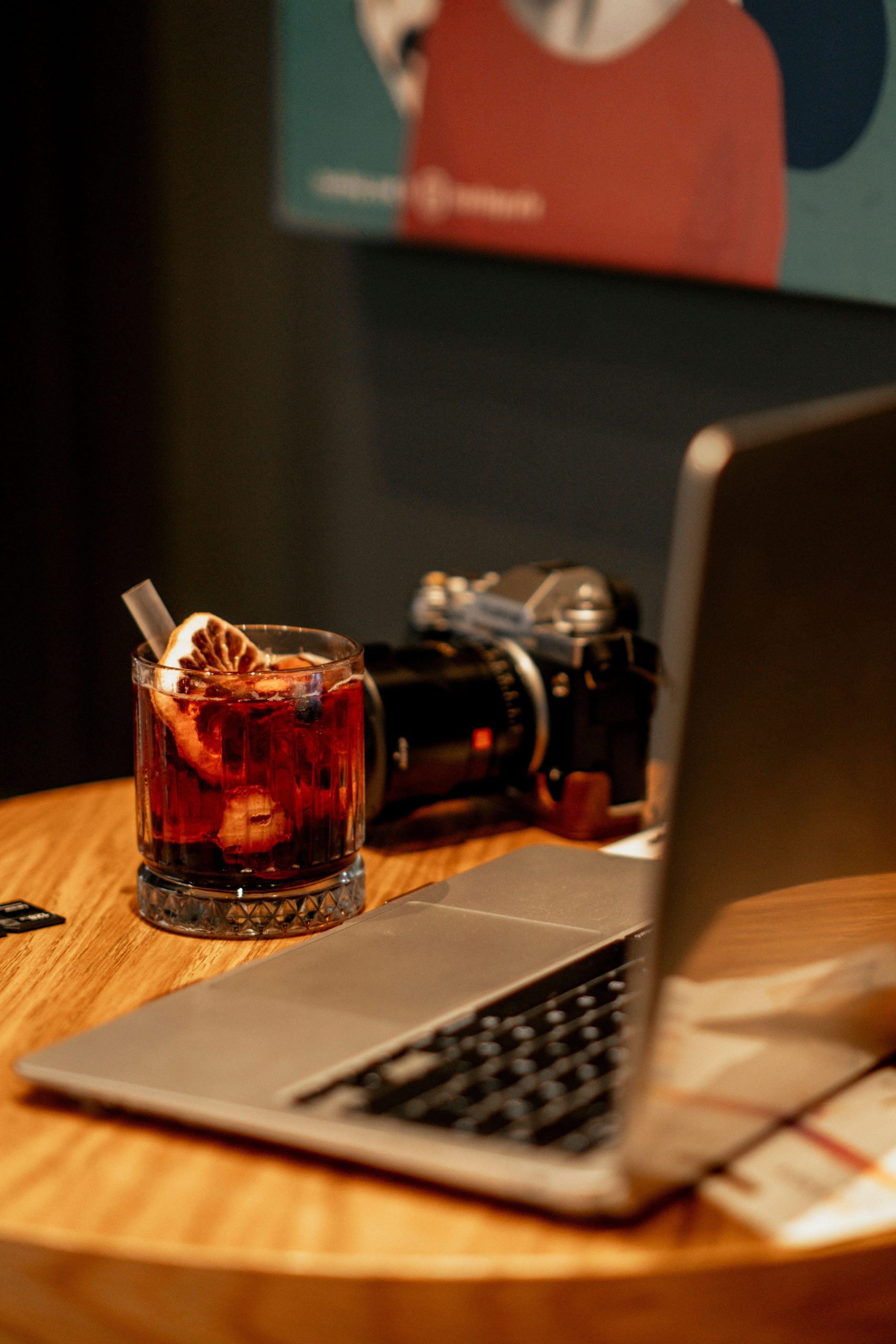 Camera and laptop beside a glass of tea on a wooden table. (Stock photo, illustrative.)