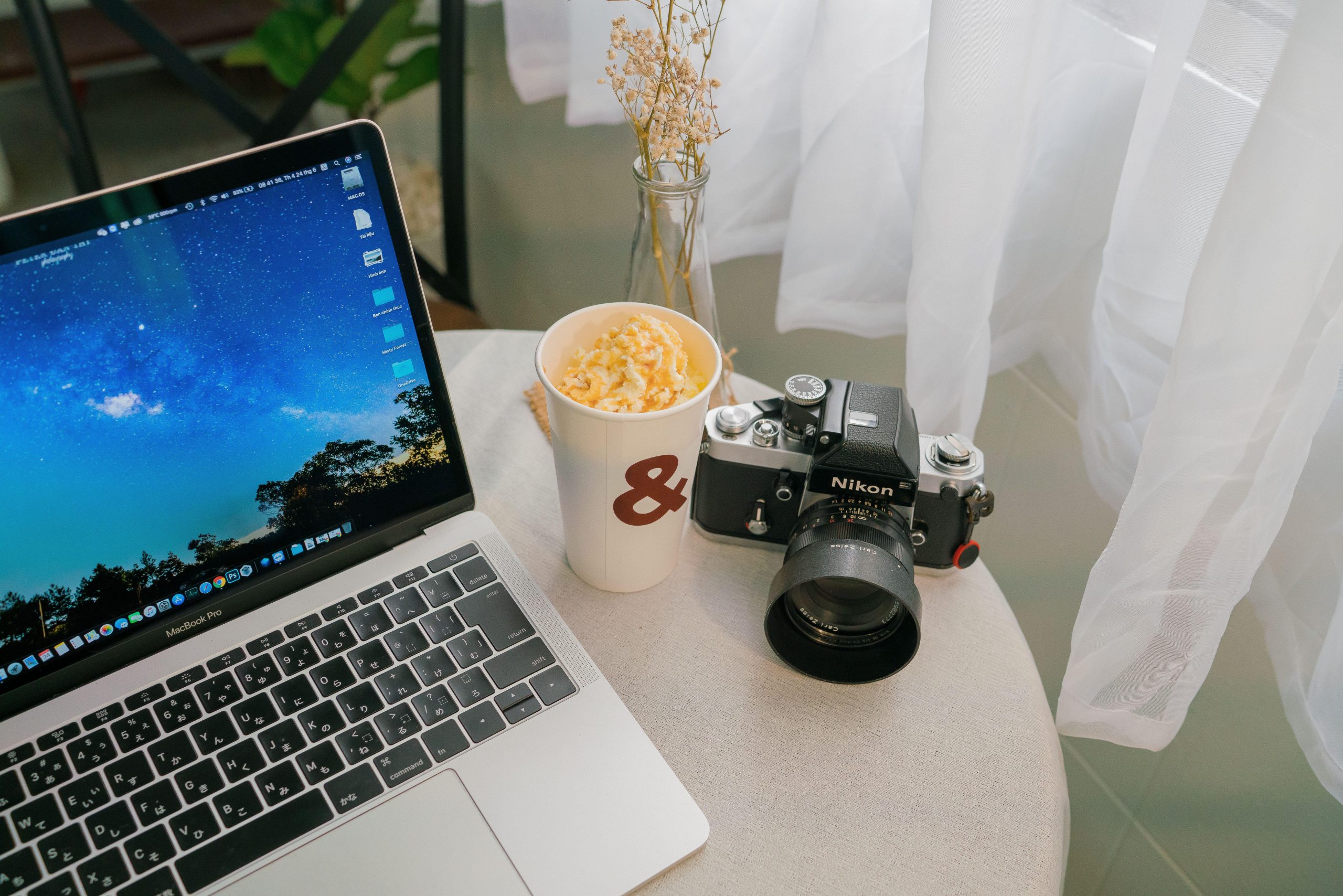 Laptop and film camera on a small table beside curtains. (Stock photo, illustrative.)