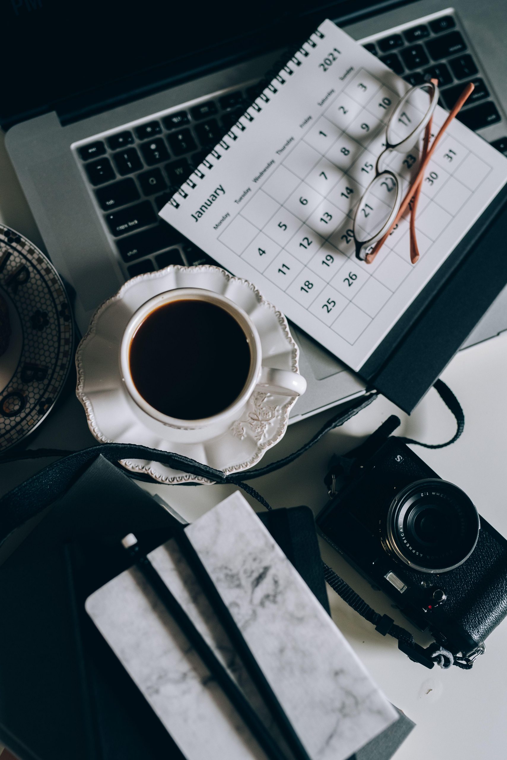Camera coffee and calendar beside a laptop. (Stock photo, illustrative.)