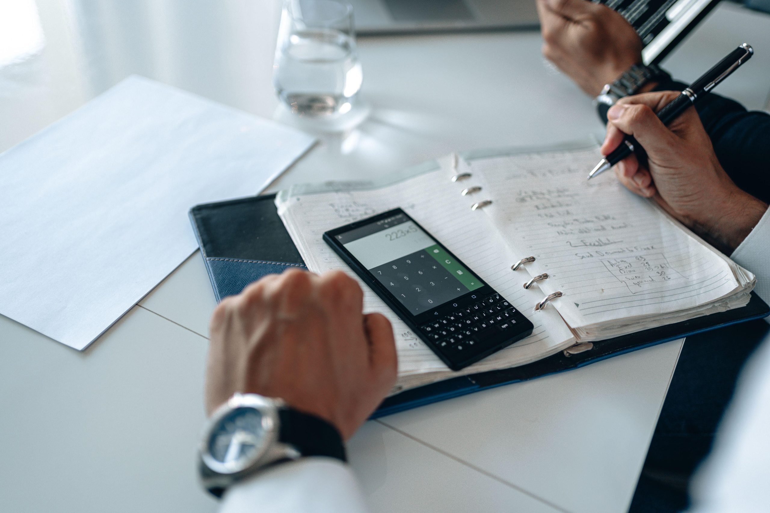 Hands using a calculator beside written business notes. (Stock photo, illustrative.)