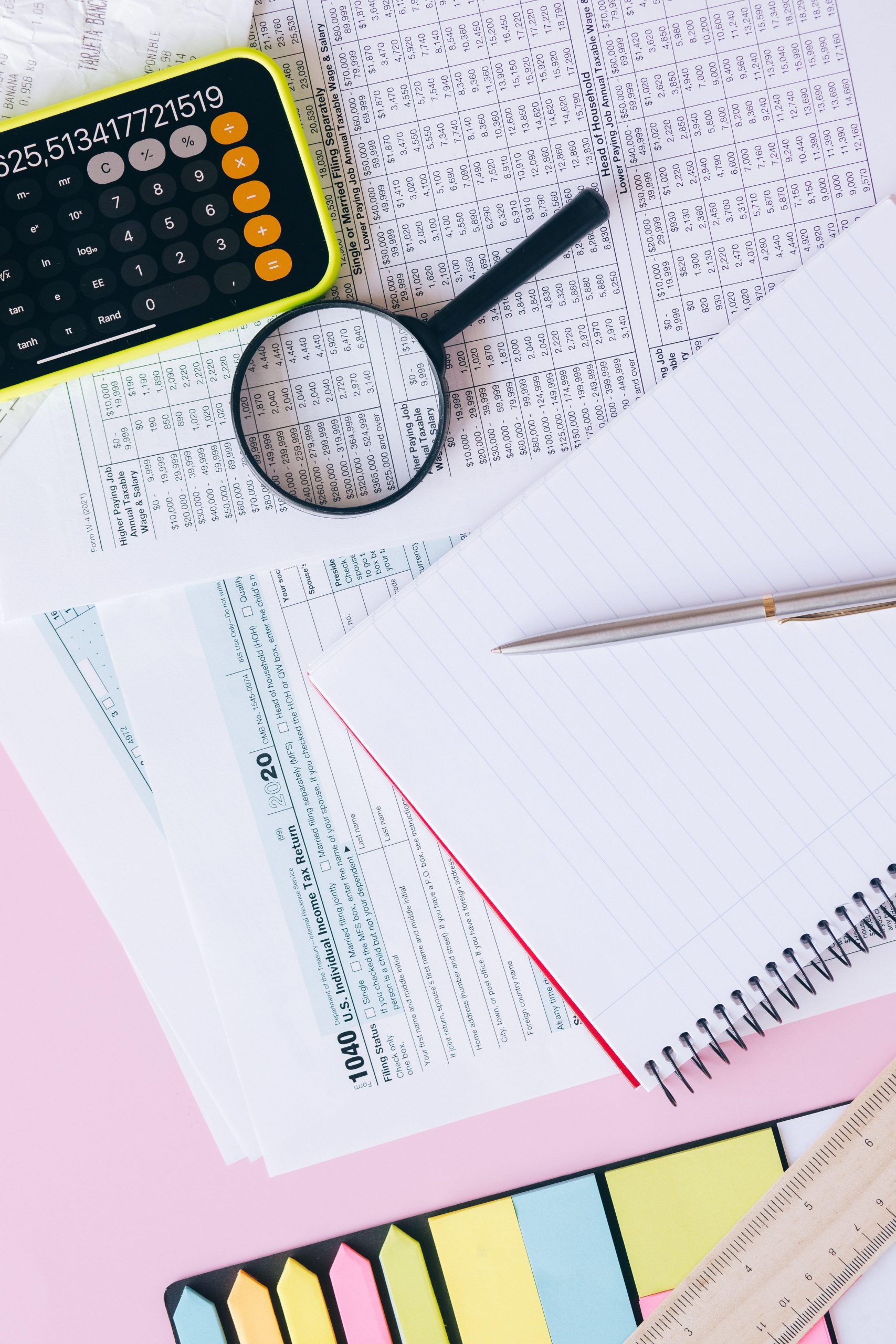 Calculator magnifying glass and financial papers on a pastel desk. (Stock photo, illustrative.)