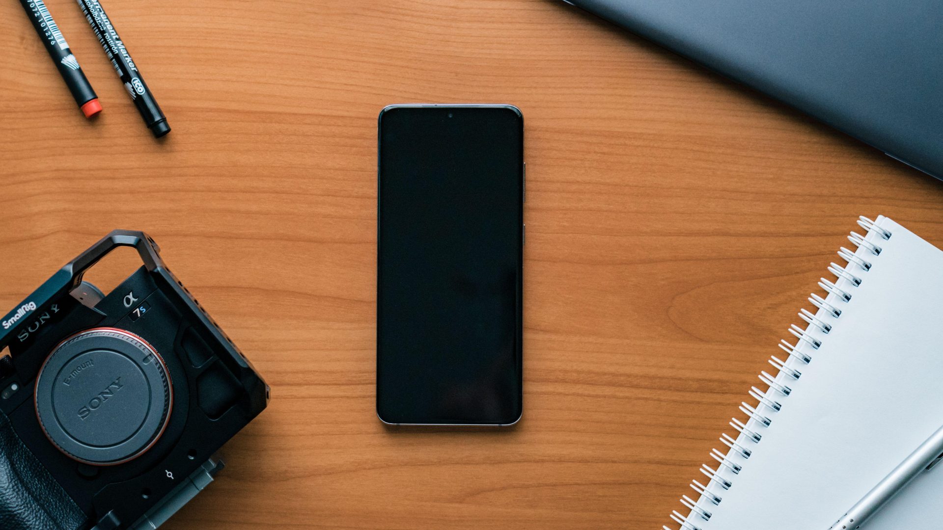Camera and phone beside a notebook on a wooden desk. (Stock photo, illustrative.)
