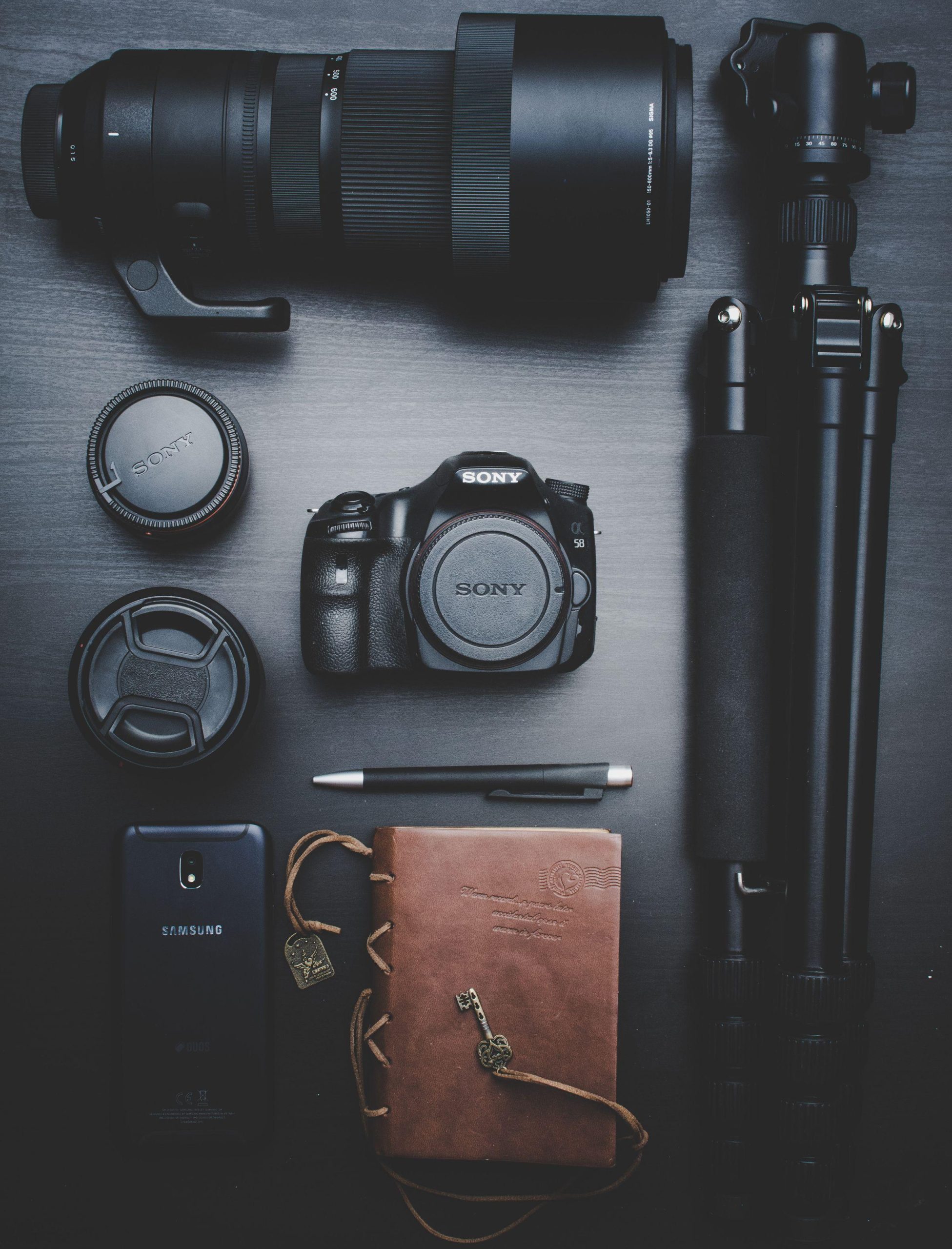 Photography camera, telephoto lens and tripod arranged on a dark tabletop. (Stock photo, illustrative.)