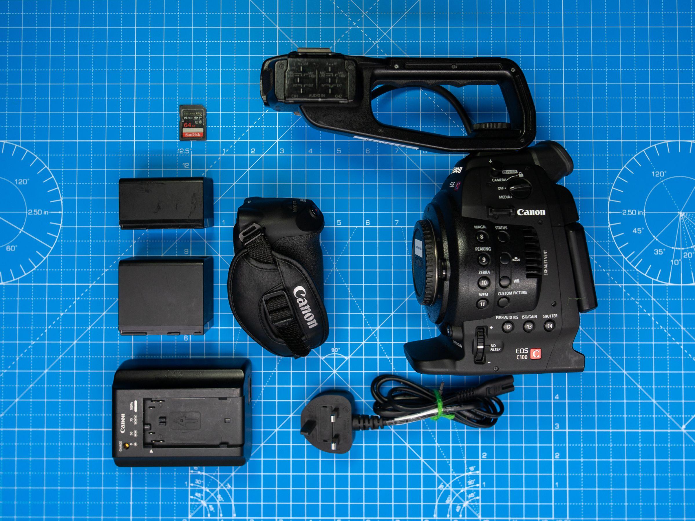 Canon cinema camera kit with batteries, charger and memory card on a blue cutting mat. (Stock photo, illustrative.)