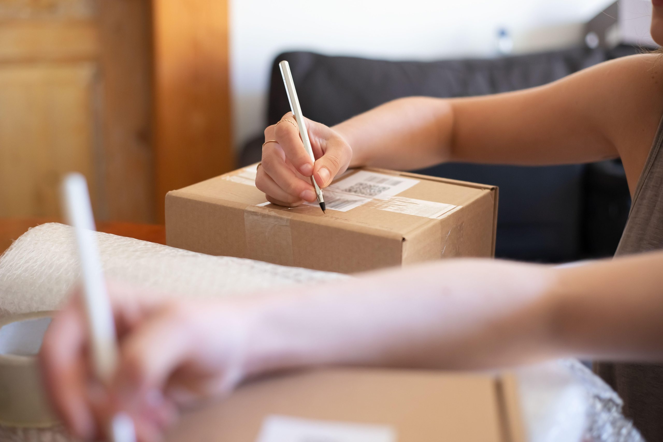 Hands labeling cardboard shipping boxes on a table. (Stock photo, illustrative.)