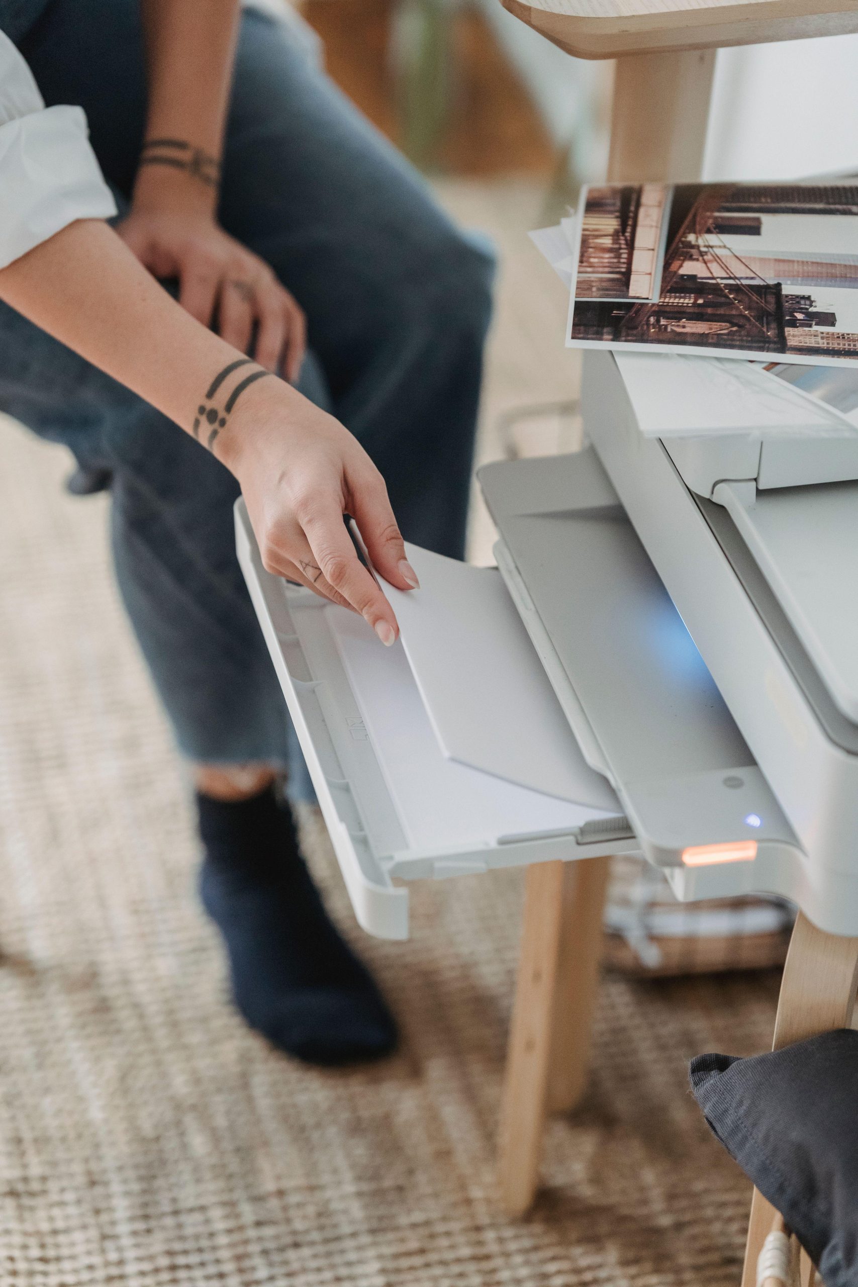 Hands loading paper into a printer beside small photo prints. (Stock photo, illustrative.)