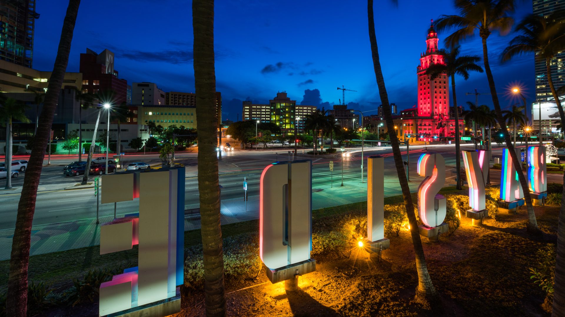 Bayside waterfront lettering, palm trees and the red-lit Freedom Tower in downtown Miami at night