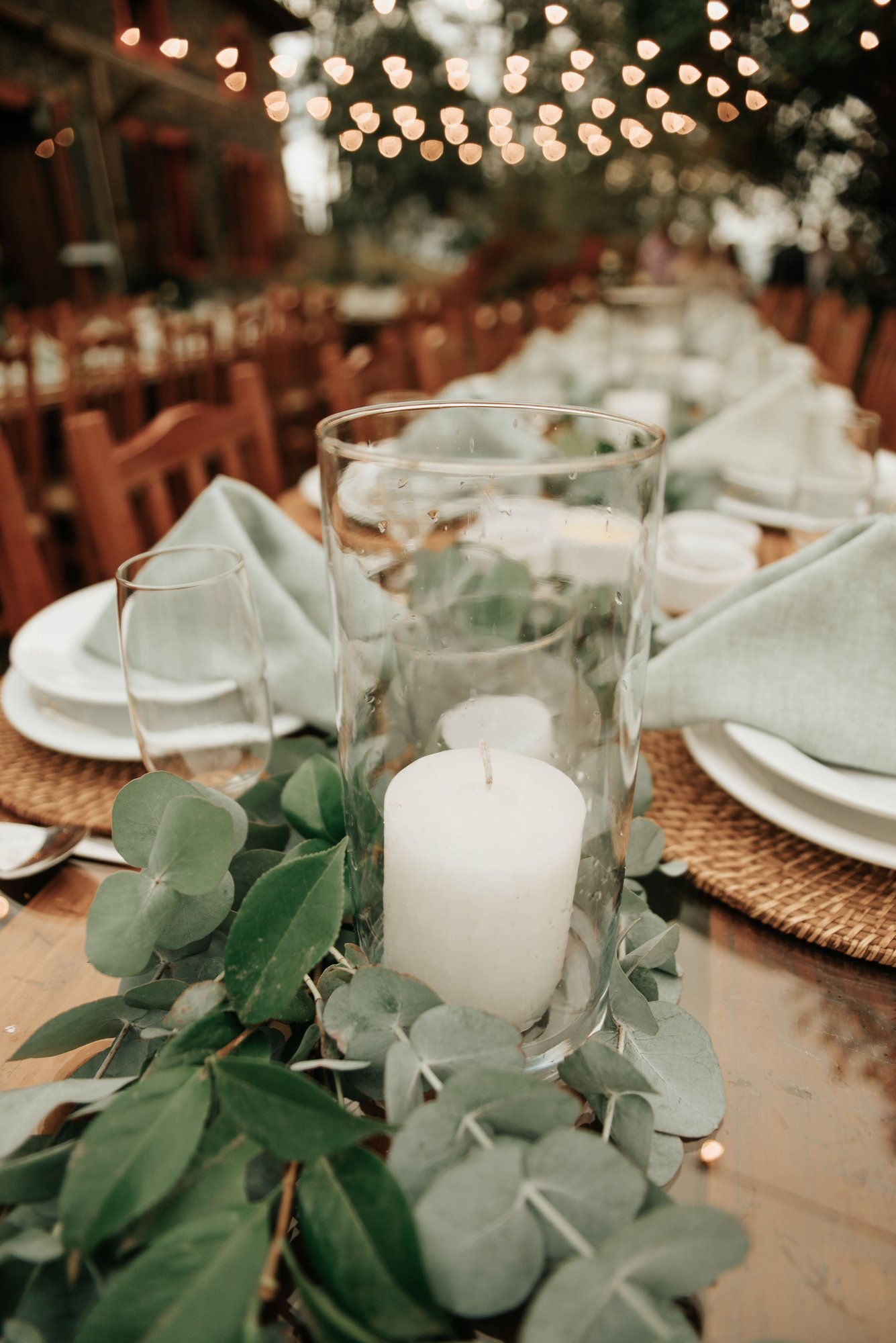 Candles and greenery on a wedding reception table with string-light bokeh. (Stock photo, illustrative.)