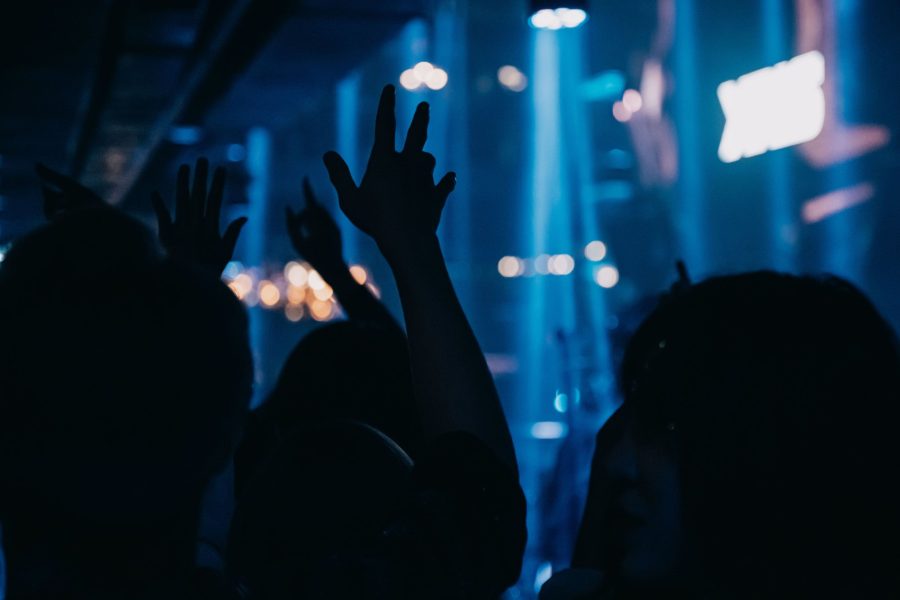 Silhouetted concert audience with raised hands under blue stage lights. (Stock photo, illustrative.)