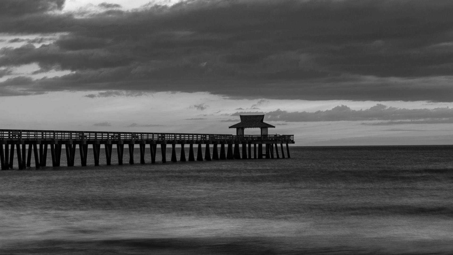 Black and white photograph of the pier at Naples, Florida, stretching over smooth water under a soft sky
