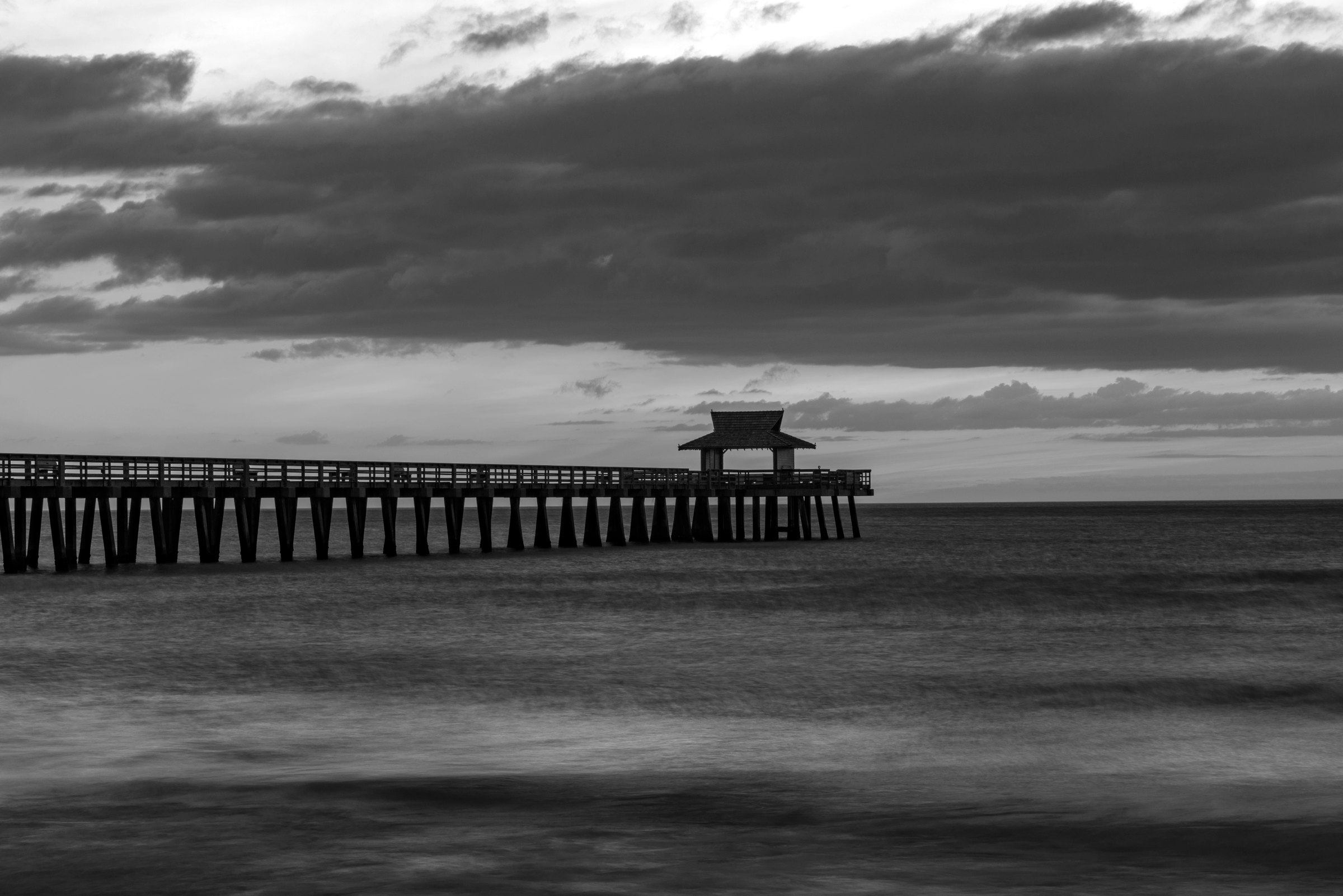 Black and white photograph of the pier at Naples, Florida, stretching over smooth water under a soft sky