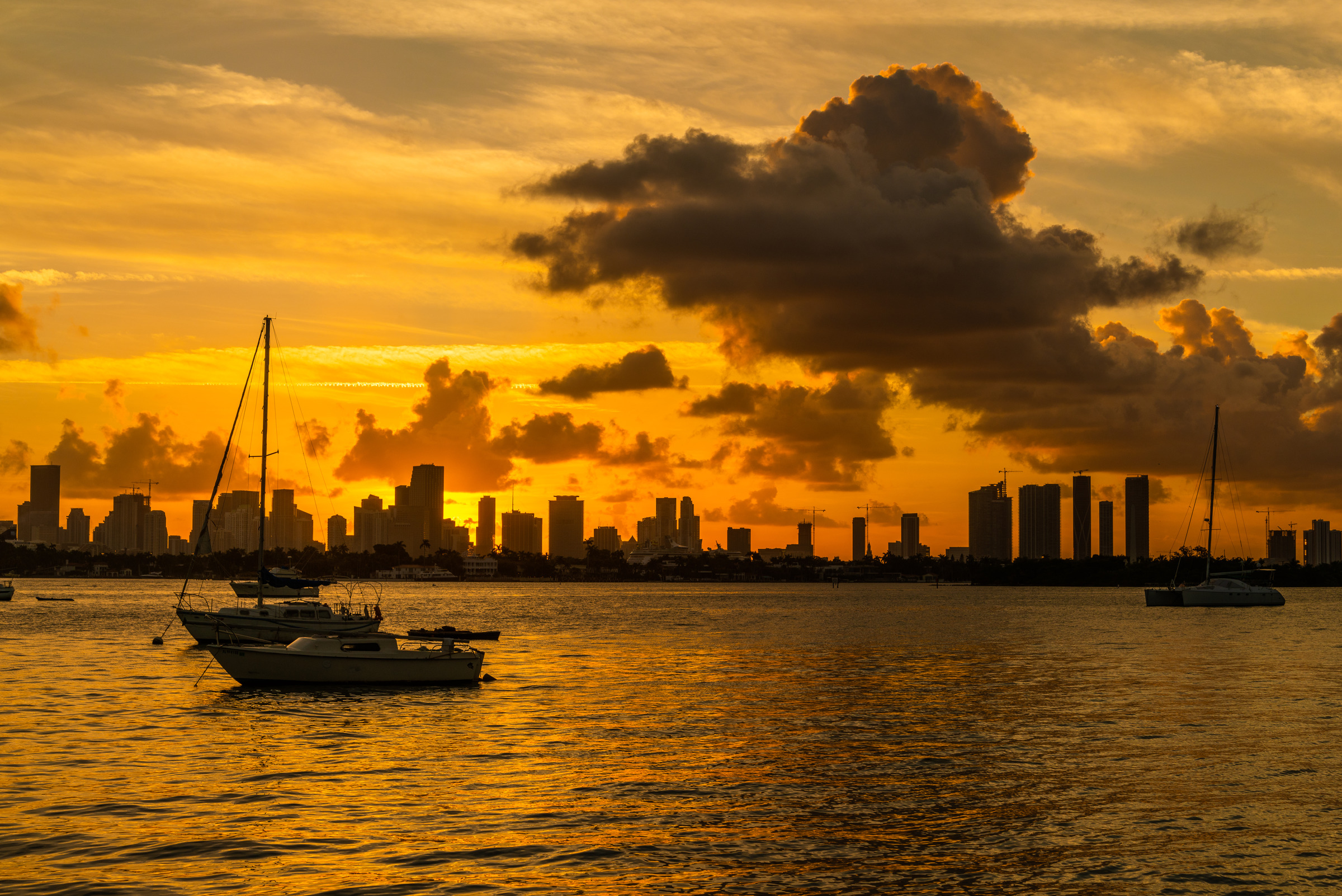 Miami skyline silhouetted against a high-contrast orange sunset with sailboats on the water