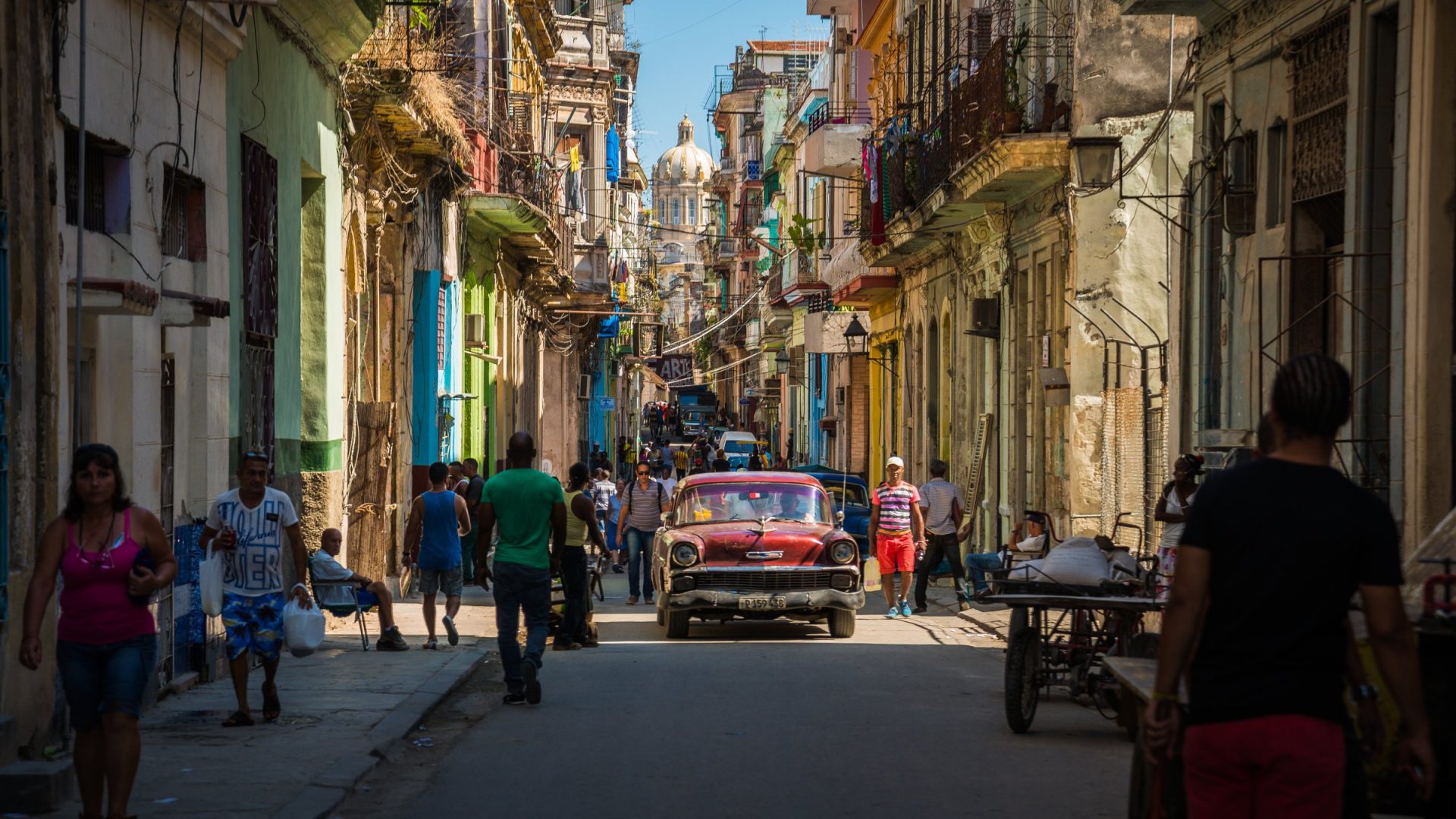 Narrow Old Havana street with pastel buildings, pedestrians and a red vintage car, Cuba