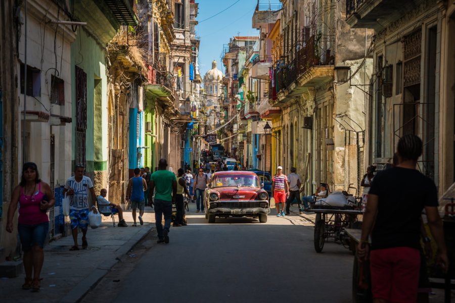 Narrow Old Havana street with pastel buildings, pedestrians and a red vintage car, Cuba
