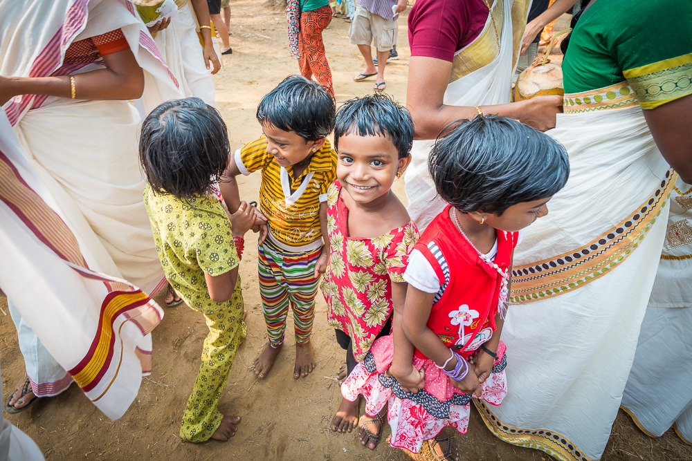 Young children in colorful clothing standing with women in white and gold saris