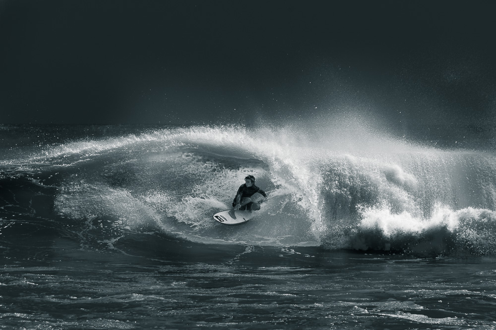 A black-and-white photo of a surfer riding inside a breaking wave