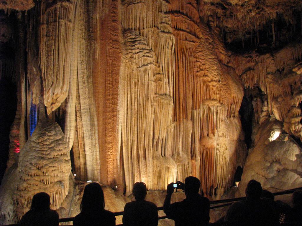 The stunning interior of the Meramec Caverns along Route 66, with towering mineral formations, strategically placed lighting, and a group of visitors marveling at the subterranean landscape.
