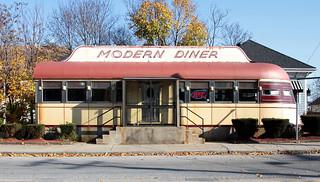 A classic American diner along Route 66, with a glowing neon sign, chrome details, and a vintage car parked outside, set against the backdrop of the open road and the vast American landscape.